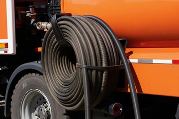 Fototapeta premium Orange utility truck with large coiled rubber hose attached to side. Used for watering plants and street cleaning tasks. Ready for municipal service.