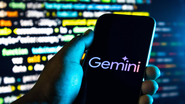 Hand holding a smartphone displaying the google gemini logo against a background of computer code