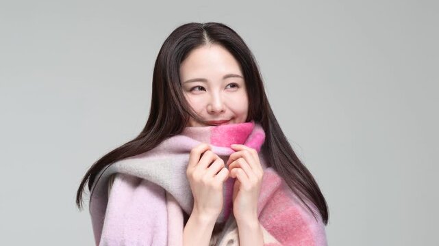 グレー背景の室内でマフラーに包まりながら笑顔を見せる30代の日本人女性
