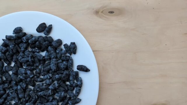 White plate filled with fresh honeyberries slowly sliding into the center on a natural wooden table in real time
