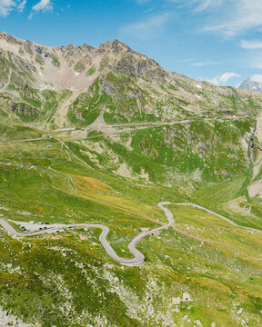 Aerial view of the Great St. Bernard Pass featuring a winding mountain road through the lush green alpine landscape of Saint-Rhemy, Valle d'Aosta, Italy.
