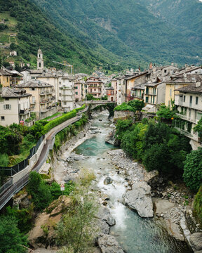 Aerial view of the historic town of Chiavenna with traditional stone buildings, the Mera river, a stone bridge, and lush green mountains in the background in Chiavenna, Lombardy, Italy.