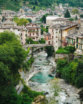 Aerial view of the historic town of Chiavenna with its stone buildings, a bridge over the Mera river, and lush greenery in Chiavenna, Lombardy, Italy.