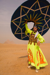 Fototapeta premium Tanoura dancer in bright neon embroidered robe raises spinning disc overhead with joyful expression before Great Pyramids of Giza ideal for cultural