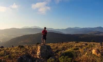 Obraz premium An 11-year-old boy with an arm brace stands on a rock, looking at mountain panorama in Crete. Inspiring travel of youth adventure, achieving goals, and overcoming physical injury during holidays