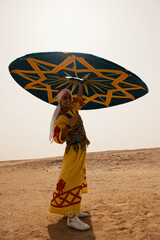 Fototapeta premium Nubian folk performer wearing vibrant embroidered yellow robe and red turban smiles while raising large geometric teal star pattern umbrella in open