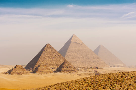 Iconic giza pyramids complex rising from the golden Egyptian desert plateau in a wide establishing landscape view with deep hazy sky and sandy