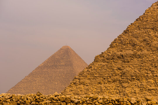 Two iconic giza pyramids layered in warm desert haze with massive ancient limestone block wall in foreground ideal for travel archaeology and world