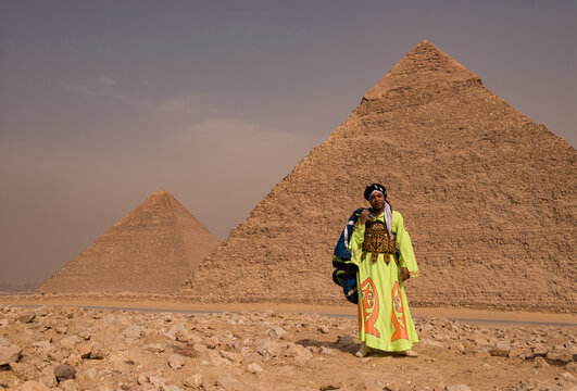 Proud Egyptian local in vibrant lime green embroidered ceremonial robe standing before iconic Giza pyramids on sandy plateau ideal for cultural