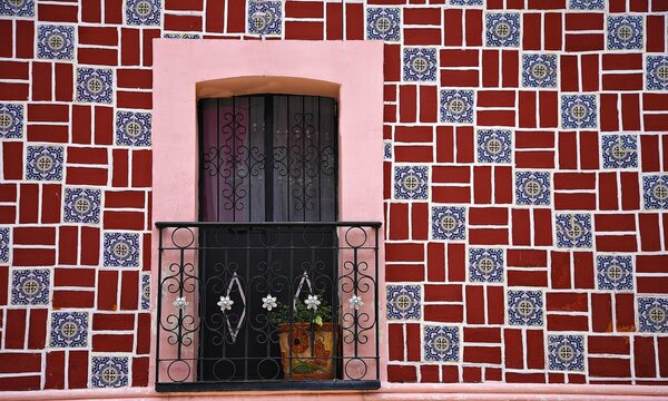 Colonial house window with a pink trim and a handcrafted wrought iron railing on a glazed Talavera ceramic tile colorful wall in Atlixco, Puebla Mexico.