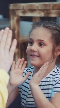 A girl with a striped shirt smiles while clapping her hands. The girl appears engaged in a playful activity with others around her in a bright setting.