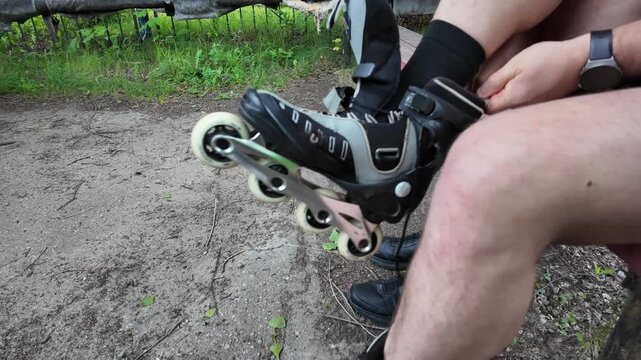 A skater eagerly sits on a bench, slipping on rollerblades in a serene park. With each strap fastened, anticipation grows for the upcoming adventure on wheels amidst nature's beauty.