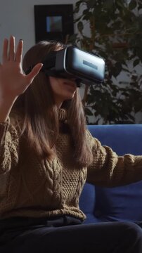 A woman wearing a virtual reality headset interacts with her environment. The woman's movements suggest she is engaged in an immersive virtual experience.