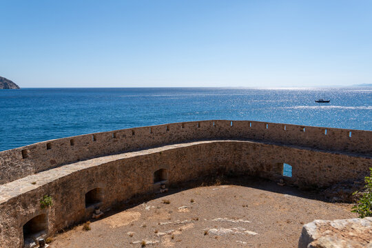 Historic stone fortress fortification with bastions and embrasures stands on coast by blue sea water under clear sky on Spinalonga island Crete Greece.