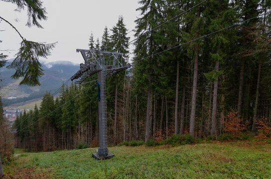 A ski lift stands at the edge of the forest on a cloudy day in a mountainous area.