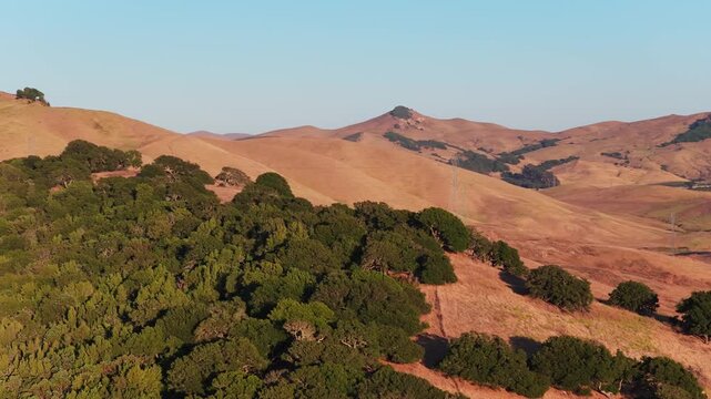 Long telephoto helix pulling out from oaks atop a ridge at sunset, revealing wave after wave of golden mountain ridgelines under a clear evening sky in Northern California.