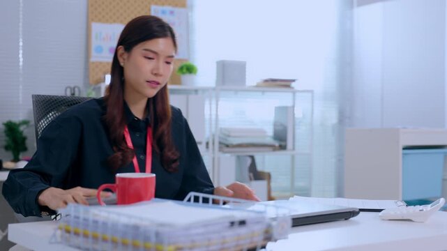 Asian woman using laptop smartphone at office desk business computer work employee professional technology with laboratory sample tube clipboard clean workplace