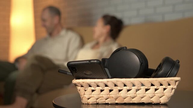 Unplugged talking on the couch without gadgets. Modern gadgets like a smartphone and headphones resting in a basket on a table while enjoys a conversation on a sofa in the background