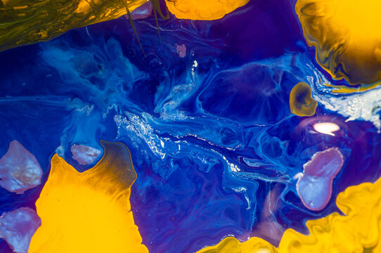 Colors mix in abstract paint on canvas with blue, yellow, and white tones in a creative space