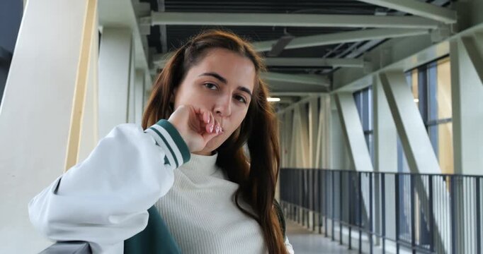Thoughtful student gazes outward. Modern student appears reflective in architectural setting. Contemplative student in varsity jacket leaning on glass barrier amidst contemporary architectural lines