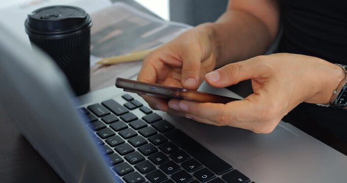 Casual multitasking scene. Individual using phone and laptop at desk with coffee and notebook. Person engaging with phone and computer while enjoying coffee in comfortable work environment