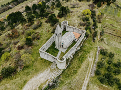 Aerial view of the historic Church of the Holy Trinity surrounded by stone walls and lush greenery in the countryside of Crni Kal, Koper, Slovenia.