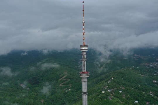 Tall communication Kok Tobe tower rises above misty forested hills under cloudy skies, Almaty, Kazakhstan