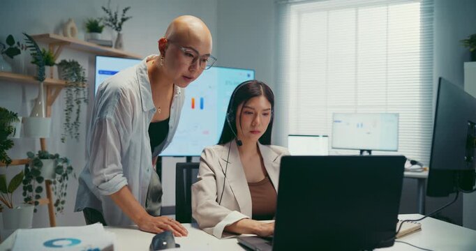 Young Asian businesswoman mentoring trainee in call center office. Corporate customer service training, employee support coach, team communication help desk, telemarketing agent work concept.