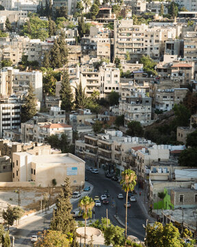 Aerial view of the dense urban cityscape of Amman with winding streets, residential buildings, and palm trees in Amman, Amman Governorate, Jordan.