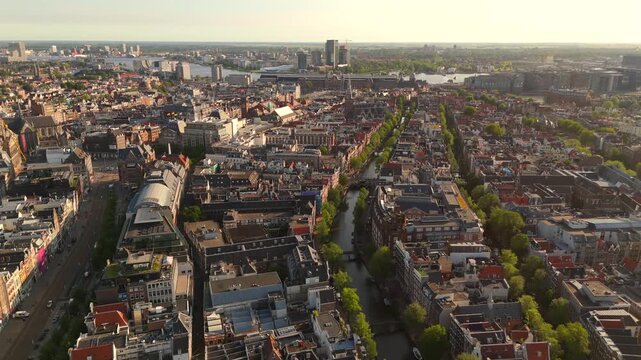 Aerial drone flies forward above Amsterdam following parallel tree lined canals extending toward the IJ waterway harbor