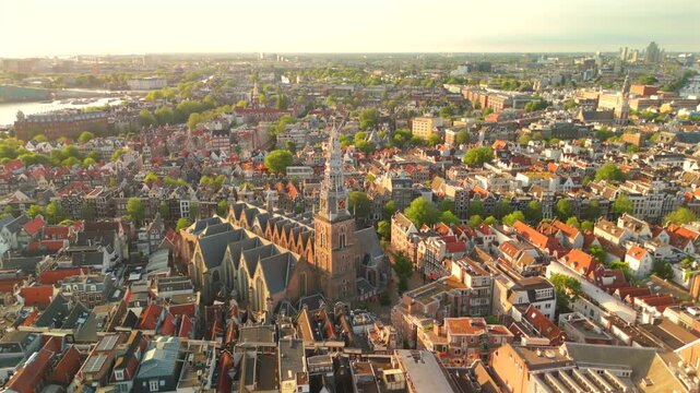 Aerial drone flies leftward above Amsterdam at golden hour featuring the prominent Oude Kerk church and red rooftops