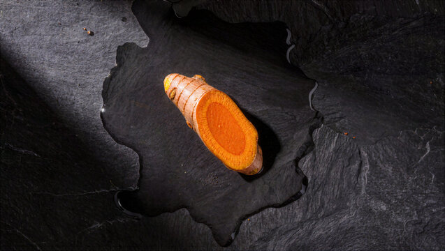 Fresh sliced turmeric root on wet black slate