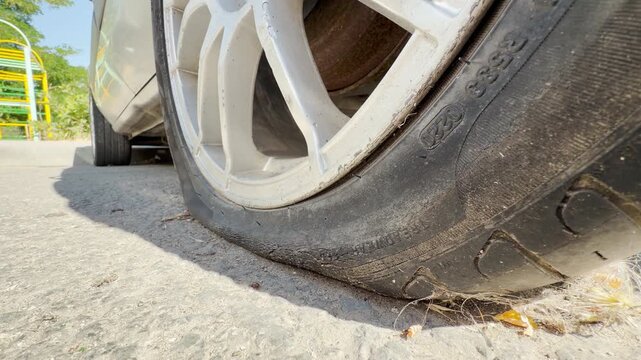 A flat car tire sits on the asphalt. This unexpected problem feels frustrating and inconvenient, leaving the driver stranded and worried about the delay.