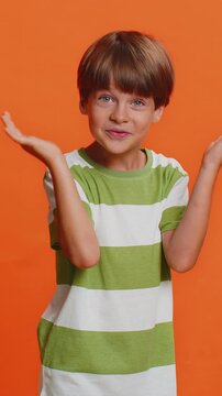 Young cute school boy 6 years old smiling friendly at camera and waving hands gesturing hello or goodbye, welcoming with hospitable expression. Preteen male child kid isolated on orange background