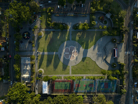 Aerial view of Alun-Alun Bangli featuring a central flower-shaped plaza, surrounding green lawns, sports courts, and lush trees in Kecamatan Bangli, Bali, Indonesia.