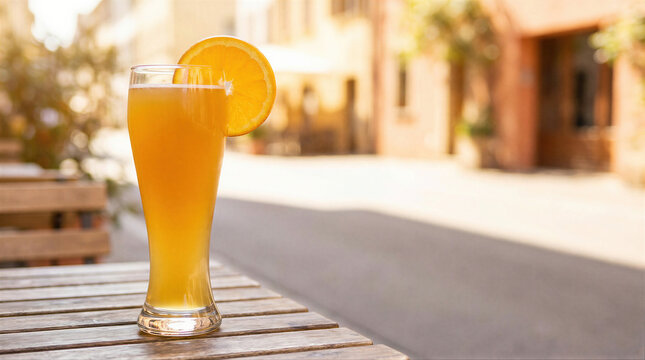 Refreshing wheat beer in a tall glass garnished with an orange slice on a wooden table. Outdoor bar terrace setting during a warm summer evening. Relaxing drink concept for vacation.