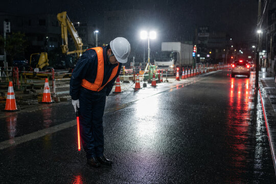 Polite traffic guard bowing with light baton at night construction site in Japan