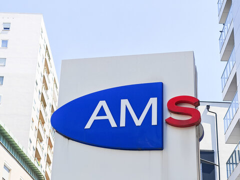 Oberwart, Austria - June 29, 2026: AMS company logo displayed on a large signboard against a clear blue sky with modern buildings in the background