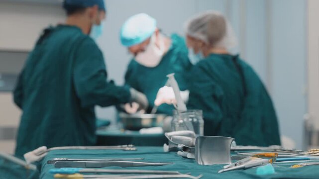 Close-up of surgical tools arranged on a sterile table while medical team operates in the background. Medical equipment, preparation and teamwork in surgery