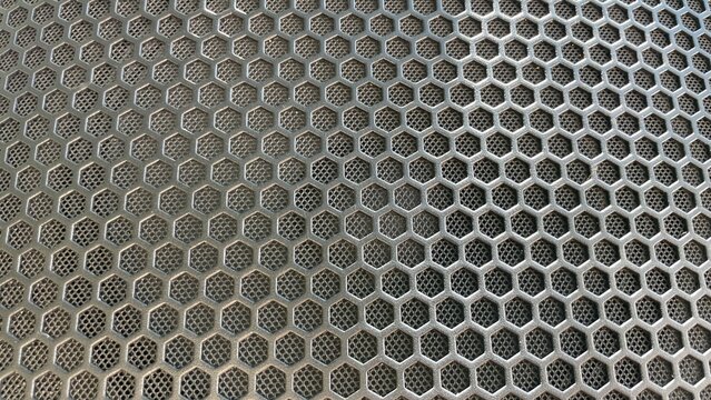 Metallic honeycomb speaker grille with hexagonal perforations creates an industrial textured surface background for audio equipment
