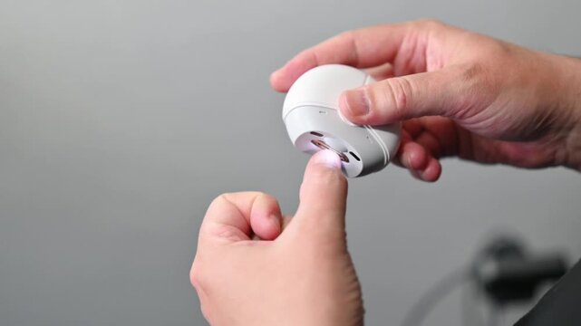 Person carefully trimming fingernails with modern electronic nail clipper device