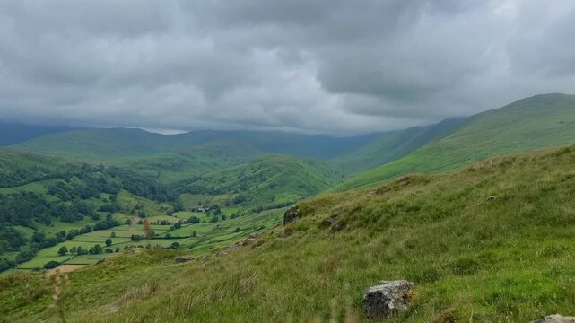 Beautiful panoramic view of a tranquil Lake District valley with rolling green hills beneath dark drifting storm clouds
