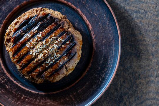 Traditional baked pastry with sesame seeds in ceramic plate. Top view freshly baked golden brown cookie or gingerbread sprinkled with white sesame seeds in rustic clay plate on wooden background