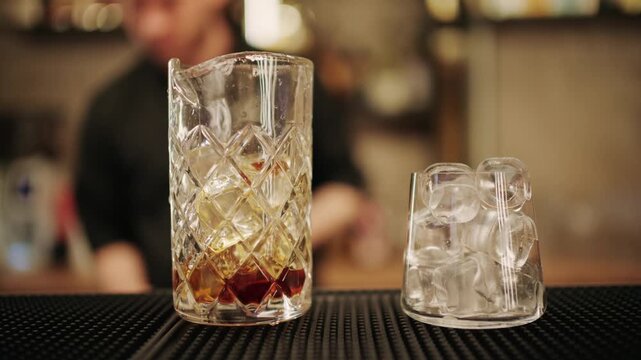 Bartender pouring red bitter and sweet vermouth into mixing glass with ice cubes for negroni cocktail.
