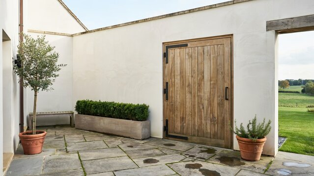 Wooden door stands within a rustic white stone courtyard featuring potted plants and flagstone flooring.