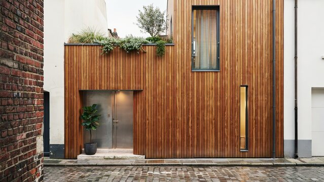 Building exterior showcases a modern facade with vertical cedar wood siding, steel entrance doors, and greenery.