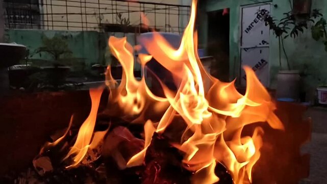 Bright orange and yellow flames engulfing burning paper or fabric outdoors at nighttime, creating dynamic fire effects.