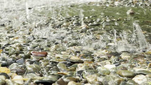 Streams of water splash dynamically onto a bed of wet pebbles. This lively movement creates a refreshing and soothing feeling in the park fountain.
