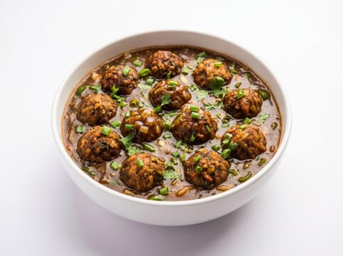 Savory Indo-Chinese veg manchurian gravy in a white bowl, featuring crispy fried vegetable meatballs in rich spicy sauce garnished with green scallions, bright clean studio food photography