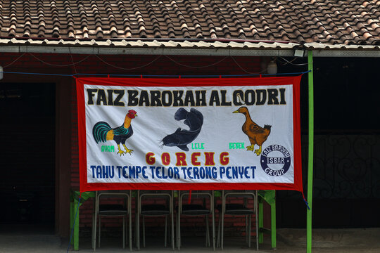 A traditional hand-painted fabric banner of a local indonesian street food stall, known as 'warung lamongan' or 'pecel lele', hanging in front of a modest eatery. the colorful banner.
